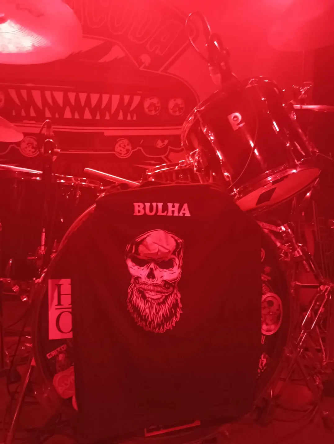 Bateria da Bulha com a tela do caveira da banda, iluminada a vermelho